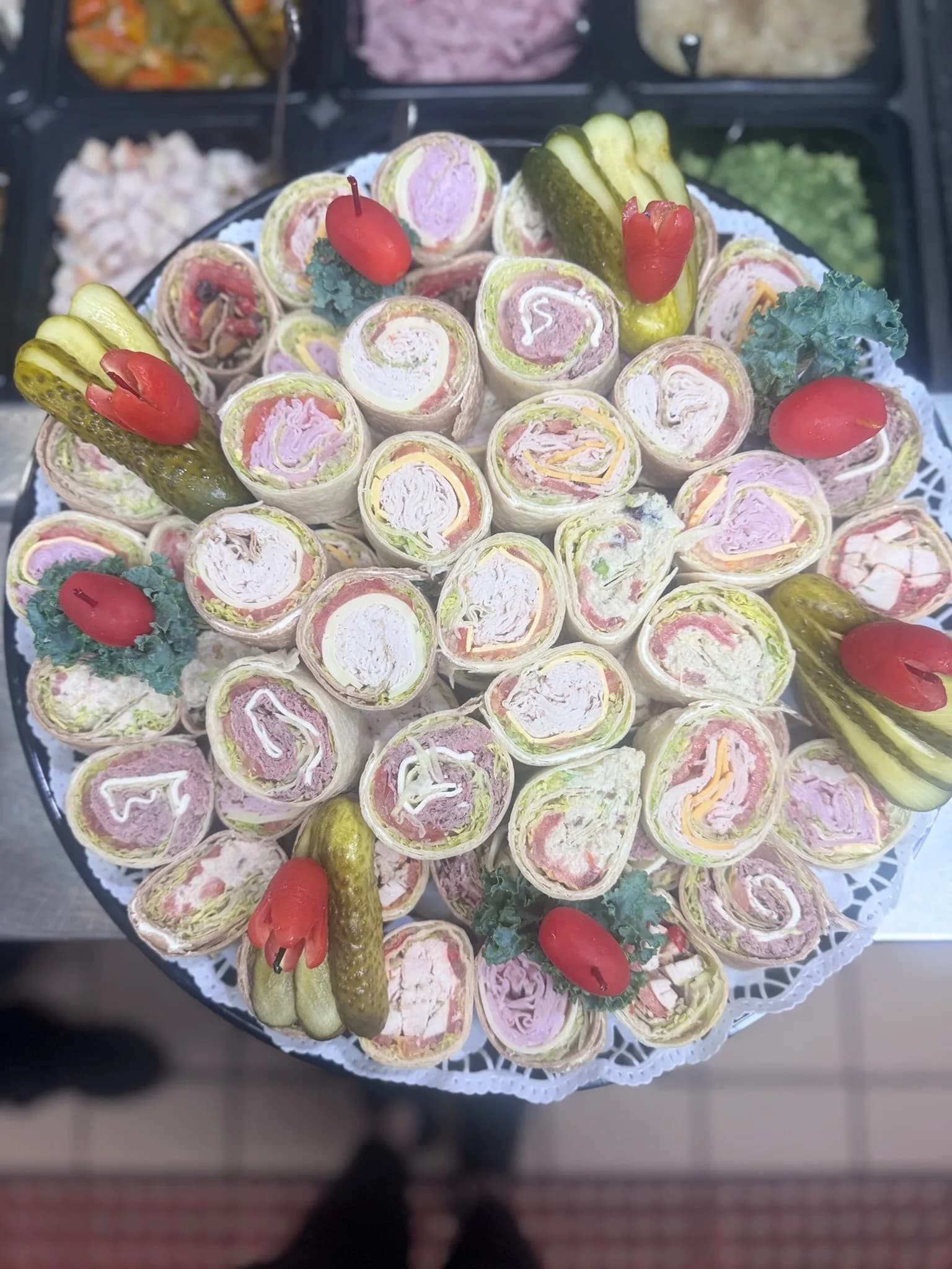 A catering platter of bite-sized wraps, garnished with pickles and tomato